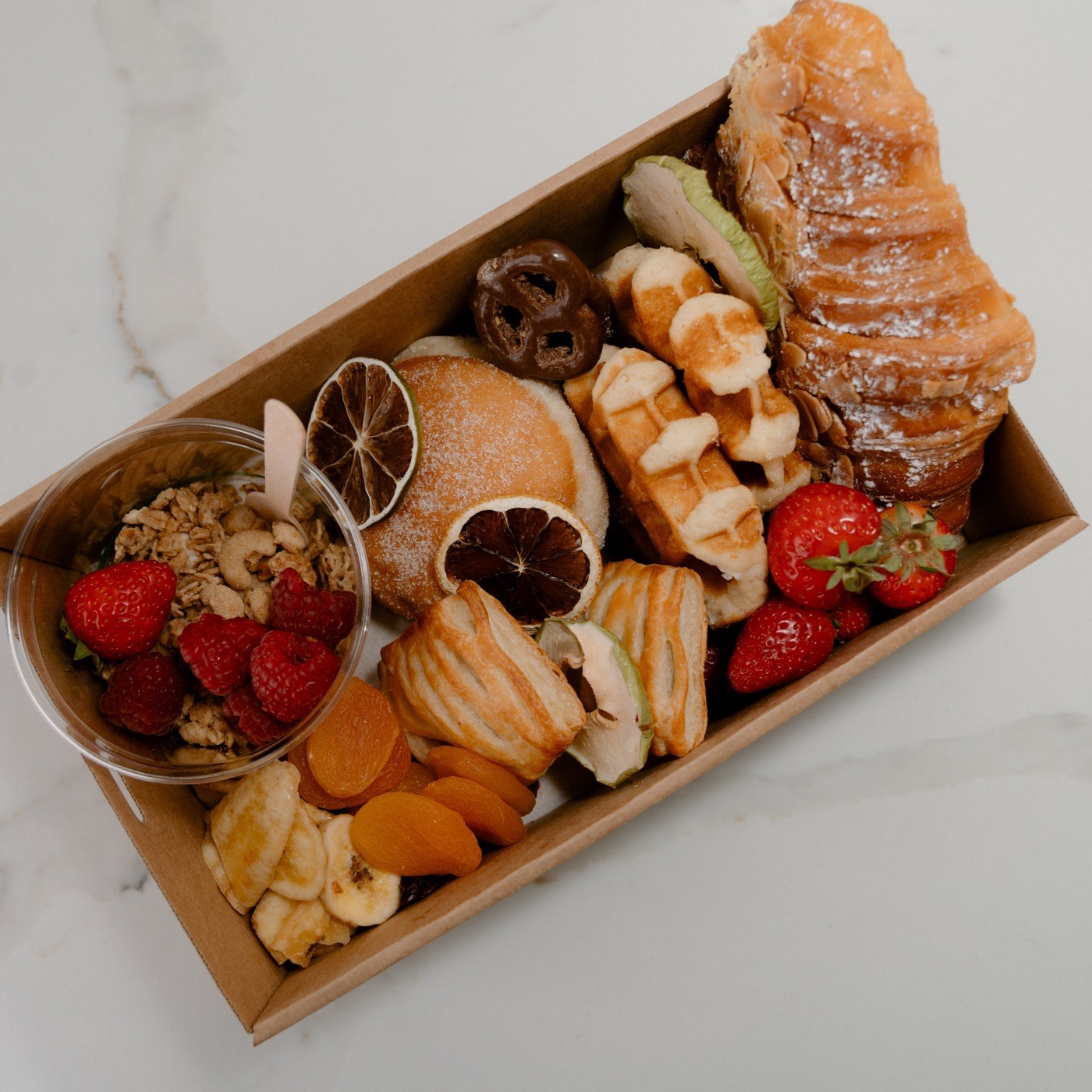 Brekky grazing box with a croissant, waffles, a granola cup, strawberries and dried fruit
