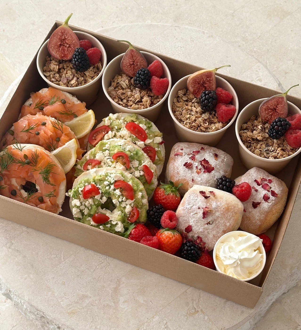 Brunch grazing box with salmon and avocado bagels, scones, granola cups and fresh berries